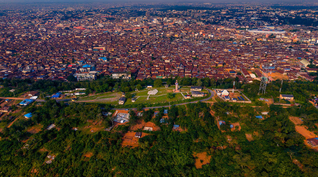 Aerial view of a modern residential estate in Ibadan, Nigeria, featuring well-planned streets, landscaped green spaces, detached homes with solar panels, and surrounding hills.