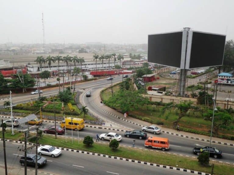Aerial view of a major road intersection in Ikeja GRA, Lagos, showing moving traffic, landscaped medians, commercial buildings, and surrounding urban infrastructure.
