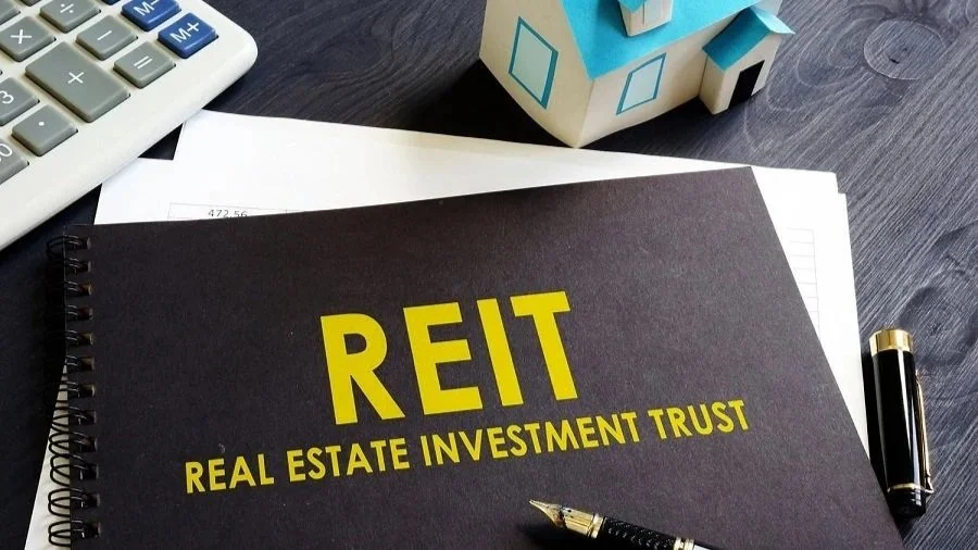 Close-up of a Real Estate Investment Trust (REIT) document beside a model house, calculator and pen, representing property investment and real estate funds.